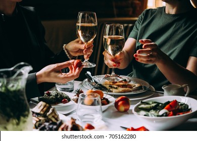 Dinner With Friends Of Family Served In A Restaurant. Two Glasses Of White Wine In Hands