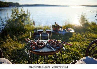 dinner in nature at sunset on the river bank, two plates of kebab and two glasses of red wine on the table - Powered by Shutterstock