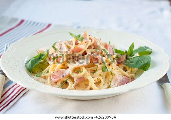 Dinner. Pasta carbonara served on deep plate\
decorated with basil\
leaves
