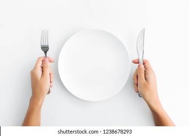 Dinner Place Setting. White Empty Plate And Hand Holding Silver Fork And Spoon On White Background, Top View, Copy Space