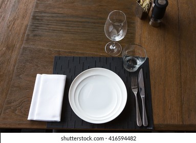 Dinner Place Setting. A White Plate With Silver Fork And Wine Glasses Isolated On Wood Table. Top View