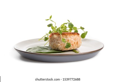 A Dinner Plate Of Crab Cake Or Fish Cake Garnished With Spinach And Pea Shoots Isolated On White