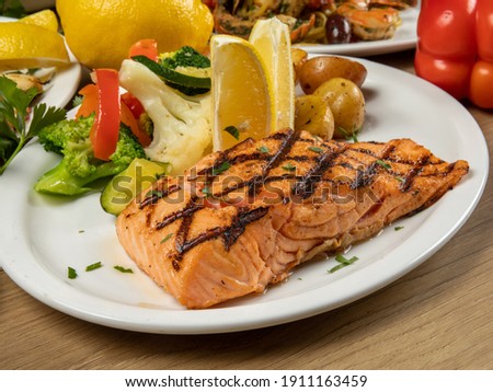 a dinner plate filled with a portion of grilled salmon filet and assorted vegetables in a restaurant setting