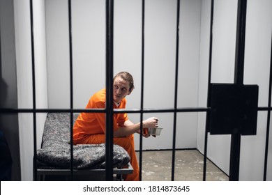 Dinner In A Prison Cell. A Prisoner Eats Tasteless Food From An Iron Bowl Under Guard Behind Bars