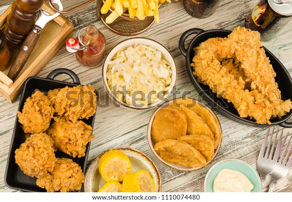 Dinner table with fried chicken wings and\
strips, roasted potatoes, french fries, coleslaw and sauces.\
Homemade southern fried chicken. Fried chicken\
meal