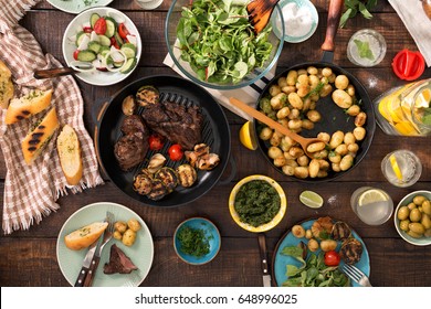 Dinner Table With Grilled Steak, Grilled Vegetables, Potatoes, Salad, Different Snacks And Homemade Lemonade, Overhead View