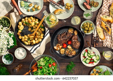 Dinner table with meat grill, roast new potatoes, vegetables, salads, sauces, snacks and lemonade, top view - Shutterstock ID 642237037