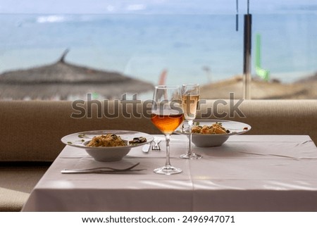 A dinner table set with two dishes of risotto, champagne, and wine. Una mesa de cena servida con dos platos de risotto, champán y vino.