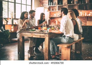 Dinning With Best Friends. Group Of Cheerful Young People Enjoying Dinner While Sitting On The Kitchen Together