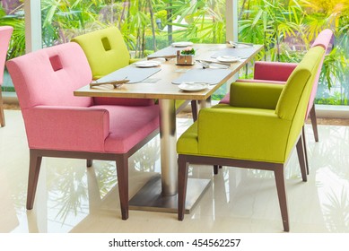 Dinning table with plates fork spoon and knife near the windows decorate with plastic flowers in restaurant at the hotel