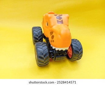 Dinosaur Monster Truck Toy, : A close-up photo of a bright orange dinosaur monster truck toy with large, black wheels.