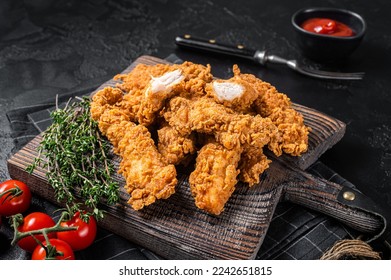 Dip fried Breaded chicken breast strips with tomato ketchup on a wooden board. Black backgrund. Top view.