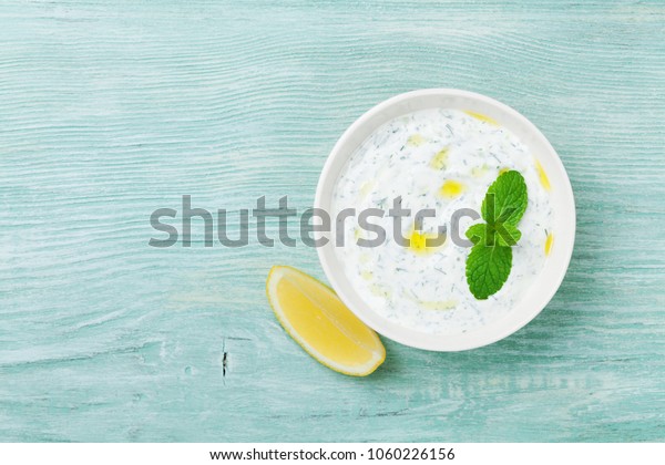 Dip sauce or dressing\
tzatziki from greek yogurt decorated with lemon, mint and olive\
oil. Top view.