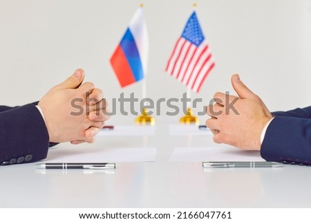Diplomatic meeting for talks between representatives of America and Russia on settlement of foreign relations. Close up of male hands, sheets of paper and pens on table on background of state flags.