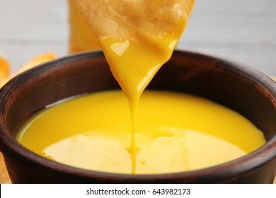 Dipping chips into bowl with creamy cheese sauce, close up