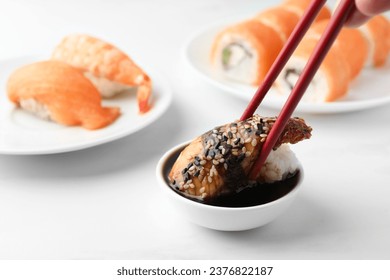 Dipping tasty nigiri sushi with smoked eel into soy sauce on white table, closeup - Powered by Shutterstock