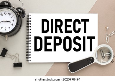 Direct Deposit. notepad on a background of different colors. brown, gray. paper clips are black and white. alarm clock near text