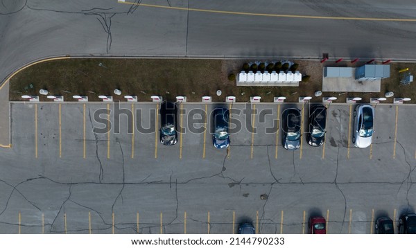 A direct\
overhead aerial view above a Tesla Supercharger station, cars are\
seen parked, charging during the\
day.