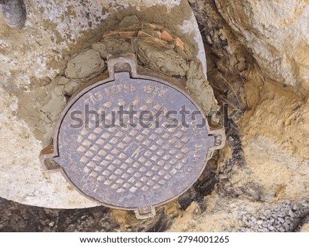 Direct overhead top down view of a closed cast iron manhole cover on the brick water supply well structure with a worker boot visible at an outdoor utility infrastructure repair and construction site.