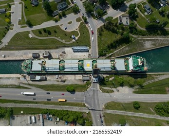 A Direct Overhead, Top-down Aerial View Of A Bulk Carrier Cargo Ship Passing Through A Tight Urban Canal At A Drawbridge Crossing During The Day.