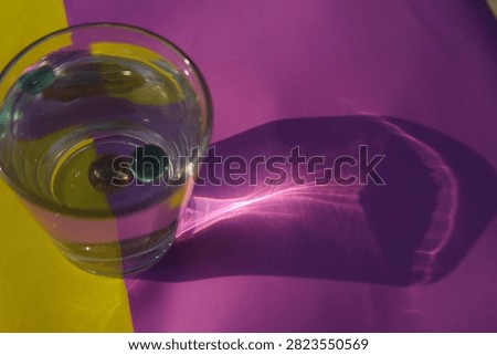 Direct Sunlight Caustic Shadow. A water glass with marbles casts a sharp caustic light refection pattern on colorful paper under bright outdoor sunlight.
