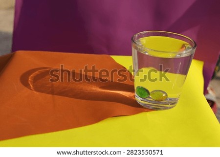 Direct Sunlight Caustic Shadow. A water glass with marbles casts a sharp caustic light refection pattern on colorful paper under bright outdoor sunlight.