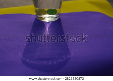 Direct Sunlight Caustic Shadow. A water glass with marbles casts a sharp caustic light refection pattern on colorful paper under bright outdoor sunlight.