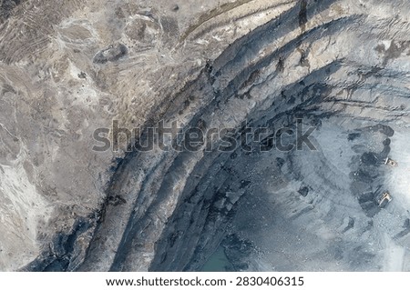 Direct top-down aerial view of a massive deep quarry amphitheater featuring sweeping curved rock benches, a small pool at the lowest floor, and heavy machinery operating on the base.