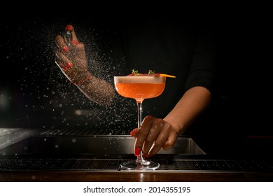 vista directa del vidrio con un delicioso cóctel espumoso brillante que la camarera de bar sostiene con la mano y le rocia. Muchas gotas alrededor