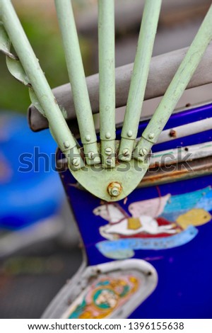 Direct view of pastel green painted five arms steel roof holder mechanism with rusty screws of old cycle rickshaw with background of flying colourful horse on blue background painting at the seating 