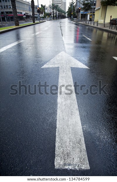 Directional arrow pointing forward on an empty wet\
street in winter\
time.