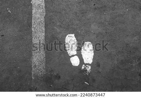 directions for pedestrians with a picture of a pair of feet on the floor in black and white in the parking lot of an office in Jakarta