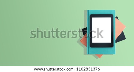 directly above shot of e-book reader, e-reader on stack of books on green desktop