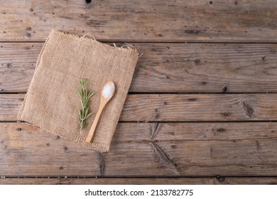 Directly Above Shot Of Rock Salt In Wooden Spoon And Rosemary On Jute Fabric At Table. Unaltered, Copy Space, Ingredient, Food, Herb, Rock Salt And Seasoning.