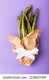 Directly above view of asparagus bunch in brown paper tied with white ribbon on purple background. unaltered, food, healthy eating and organic concept.