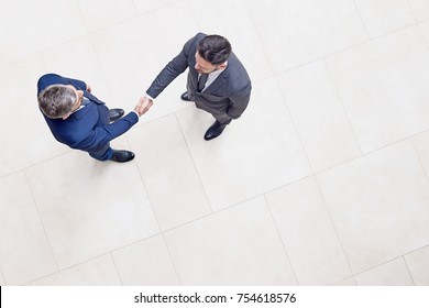 Directly above view of confident business partners in classical suits shaking hands after successful completion of negotiations, interior of office lobby on background - Shutterstock ID 754618576