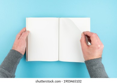 Directly Above View Of Person Turning Page Of Blank White Page Hardcover Book On Blue Background