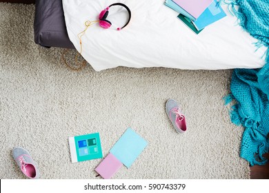 Directly Above View Of Teen Girl Messy Bedroom With Blanket, Sneakers And School Books Scattered On Carpet