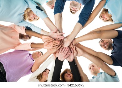 Directly Below Creative Business Team Stacking Hands While Standing In Huddle Against White Background