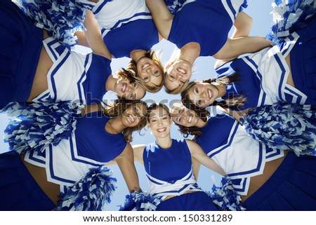 Directly below shot of happy cheerleaders forming huddle against sky