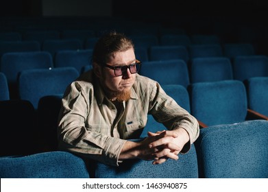 Director By One In Dark Theater Hall. Portrait Of Creative Man In Low Key. Alone Art Person In Concert Hall. Surprised Critic At Premiere. Happy Brutal Bearded Man With Glasses In Culture House.