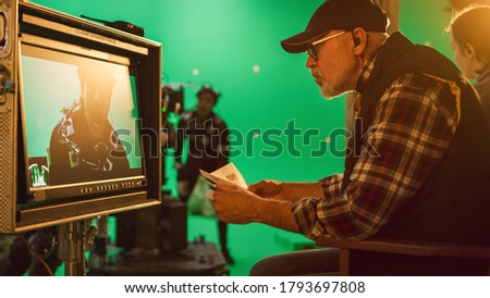 Director Looks at Display and Compares to Storyboard while Shooting Blockbuster Movie. Green Screen Scene with Actor Wearing Motion Caption Suit. Film Studio Professional Crew Doing High Budget Movie