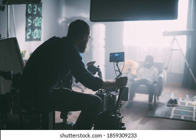 Director of photography with a camera in his hands on the set. Professional videographer at work on filming a movie, commercial or TV series. Filming process indoors, studio