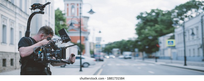 Director of photography with a camera in his hands on the set. Professional videographer at work on filming a movie, commercial or TV series. The filming process on the street, on location - Shutterstock ID 1881731584