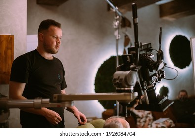 Director Of Photography With A Camera In His Hands On The Set. Professional Videographer At Work On Filming A Movie, Commercial Or TV Series. Filming Process Indoors, Studio