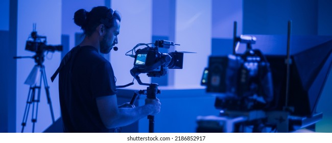 Director of photography with a camera in his hands on the set. Professional videographer at work on filming a movie, commercial or TV series. Filming process indoors, studio - Shutterstock ID 2186852917