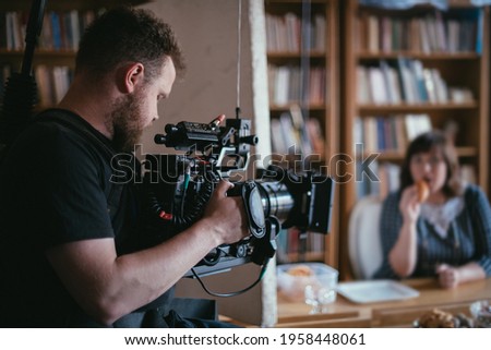 Director of photography with a camera in his hands on the set. Professional videographer at work on filming a movie, commercial or TV series. Filming process indoors, studio