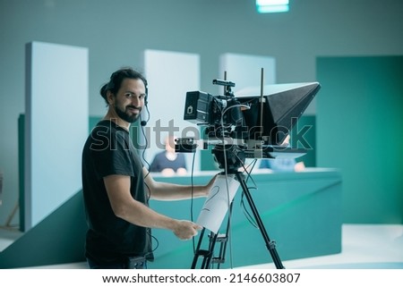 Director of photography with a camera in his hands on the set. Professional videographer at work on filming a movie, commercial or TV series. Filming process indoors, studio