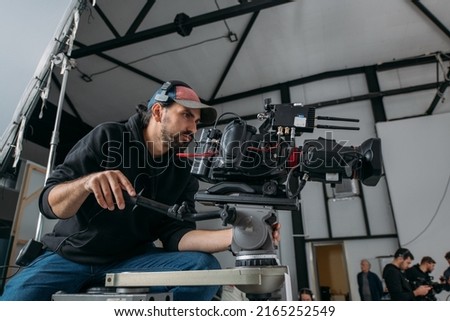 Director of photography with a camera in his hands on the set. Professional videographer at work on filming a movie, commercial or TV series. Filming process indoors, studio