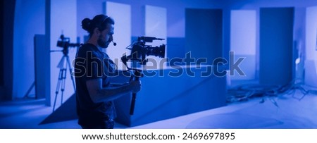 Director of photography with a camera in his hands on the set. Professional videographer at work on filming a movie, commercial or TV series. Filming process indoors, studio